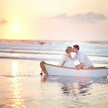 Молодожёны на свадебной фотосессии в лодке на фоне заката у моря