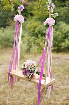 Букет невесты на украшенных лентами свадебных качелях на фотосессии в Минске